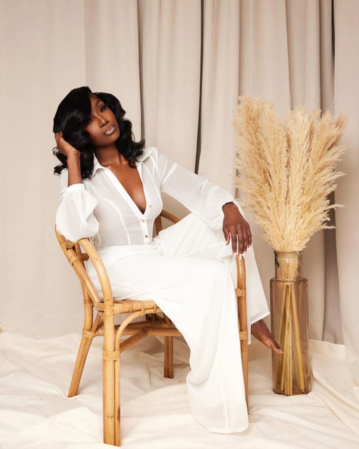 Editorial portrait of a woman in a white outfit seated beside dried grasses